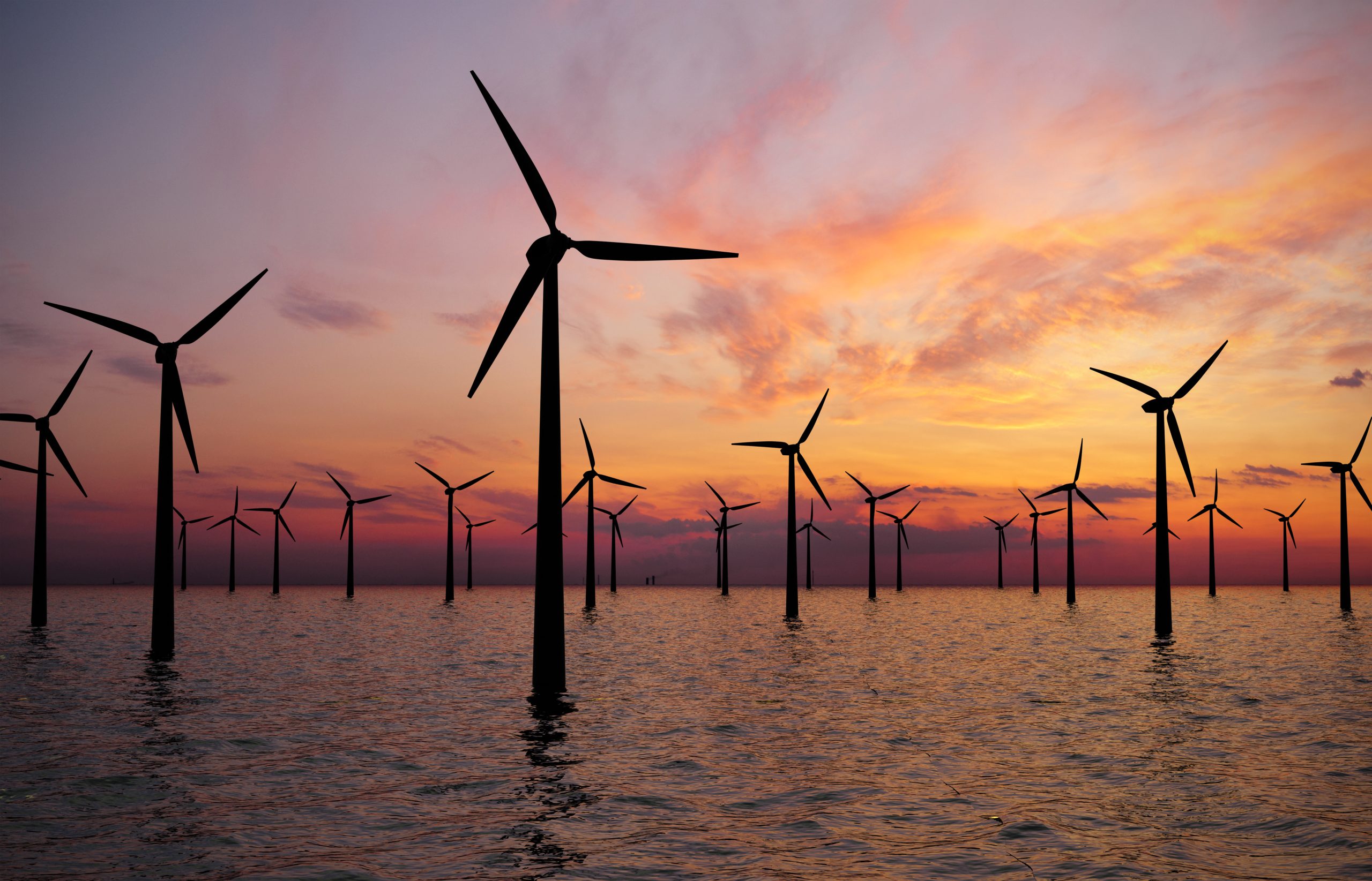 Offshore wind turbines at sunset over the sea.