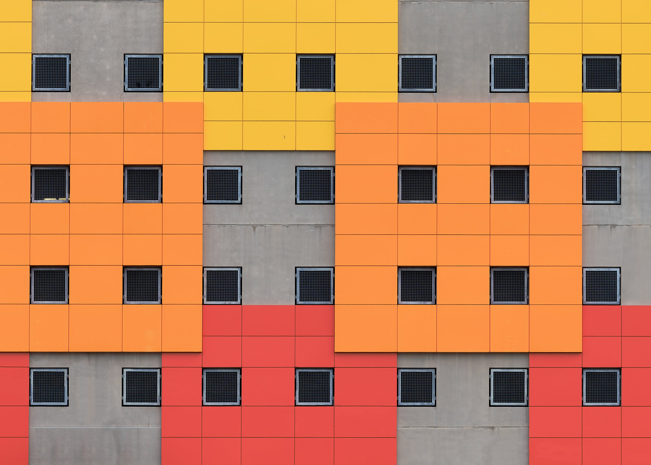 Colourful building facade with yellow, orange and red square panels and small grid windows arranged in a geometric pattern.