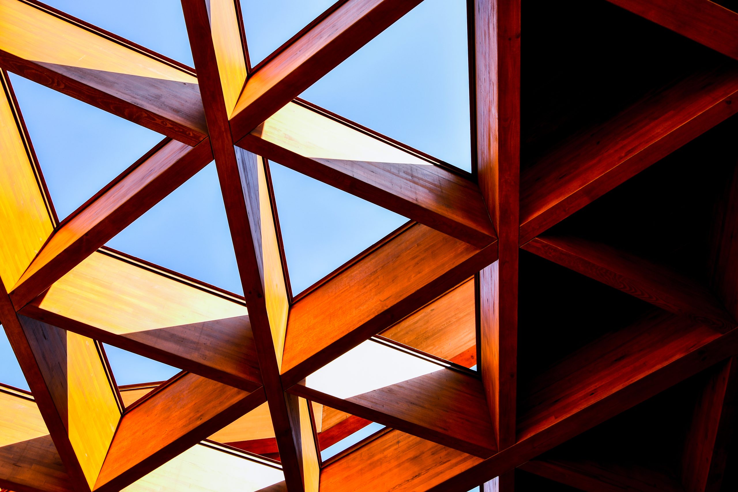 Abstract geometric wooden roof structure with triangular openings showing blue sky
