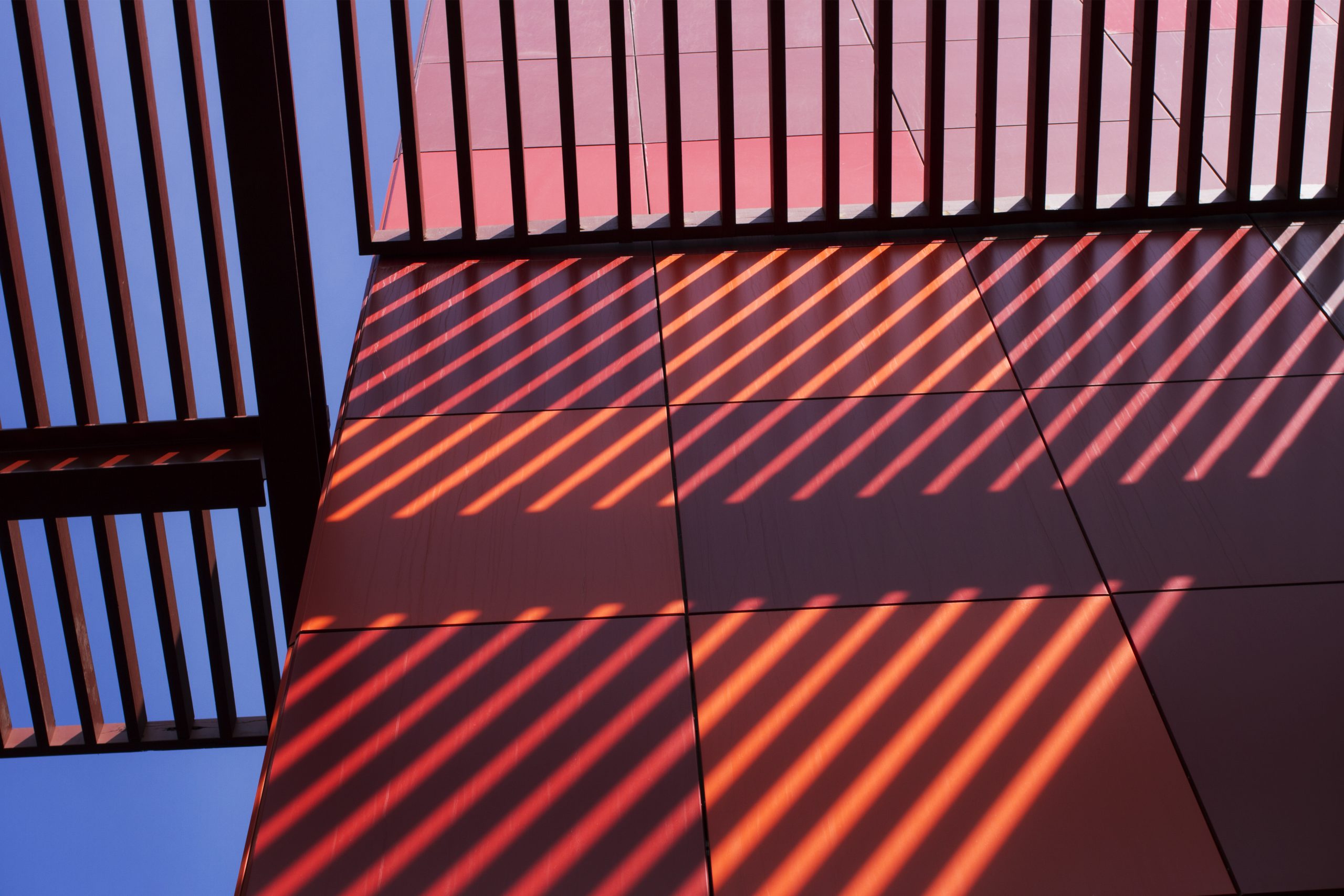 Abstract architectural shadows falling across a modern red building facade